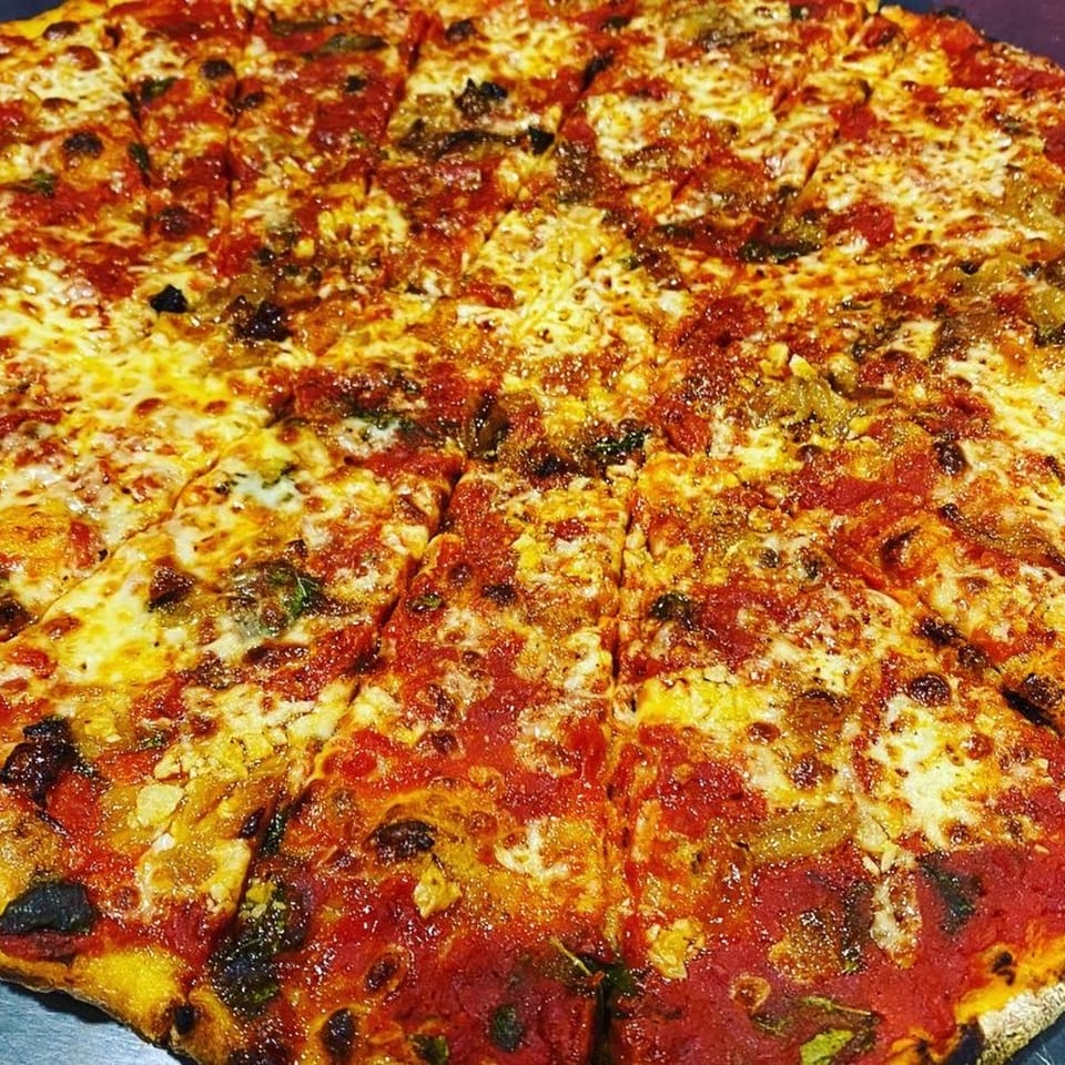 A close-up of a freshly baked, sliced Casa Pizzeria craft pizza with melted cheese and red sauce.