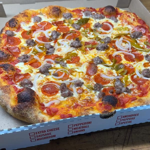 A Casa Pizzeria craft pizza with pepperoni, sausage, onions, and green peppers in a box.