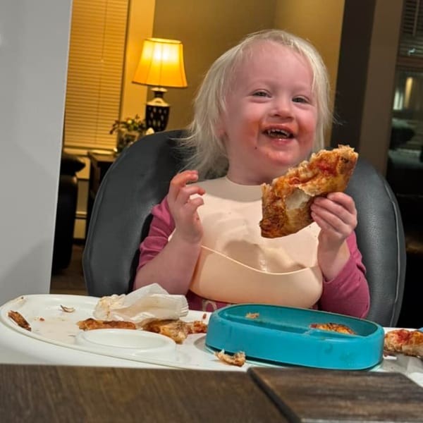 A happy child with sauce on their face, holding a slice of Casa Pizzeria's craft pizza.