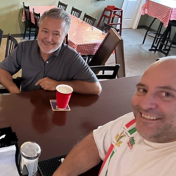 Two men smiling at the camera from a bar counter inside Casa Pizzeria.