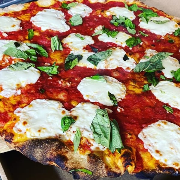 Close-up of a Casa Pizzeria Margherita pizza with fresh mozzarella, vibrant tomato sauce, and basil.